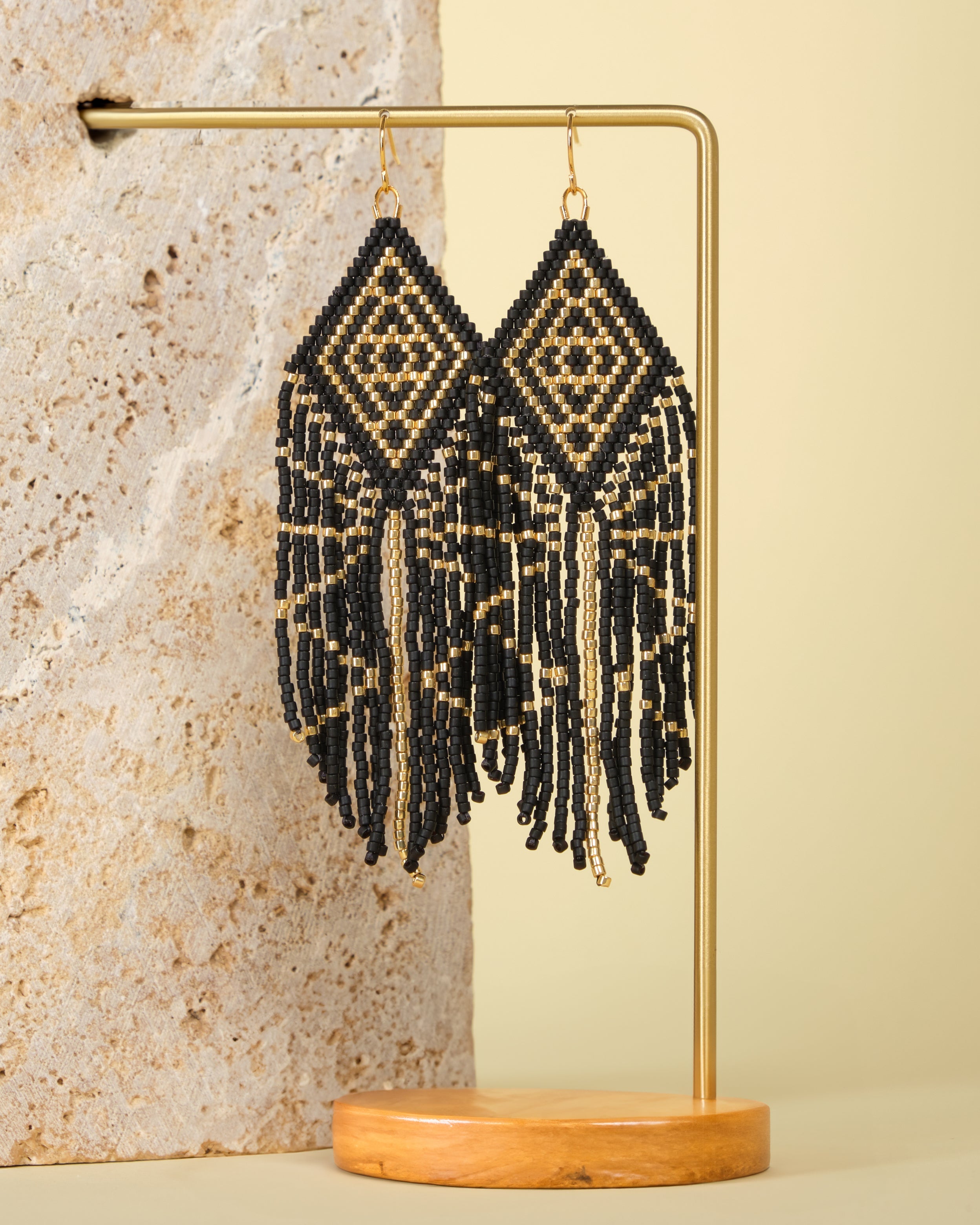 Tribal Diamond Fringe Earrings in Black/Gold – Elegant beaded earrings displayed on a textured jewelry stand