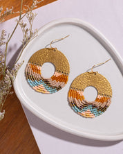 lose-up of Mayana Designs Earth Ombre Fringe Disk Earrings, highlighting the intricate beaded fringe in ombre colors and hammered brass arch.