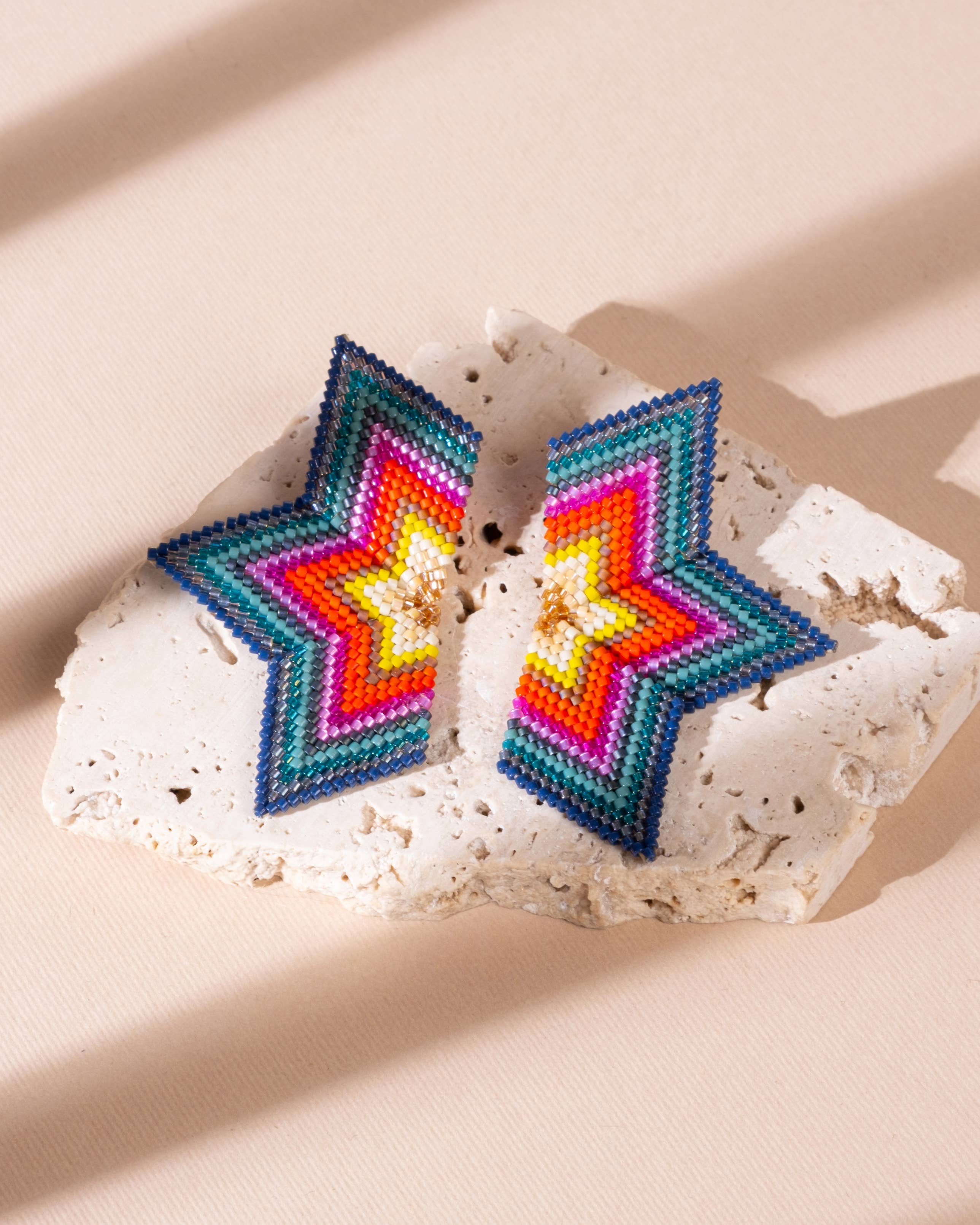 Close-up of a pair of large, red and emerald beaded earrings in a half-star shape, with vibrant beads creating a stunning gradient effect.