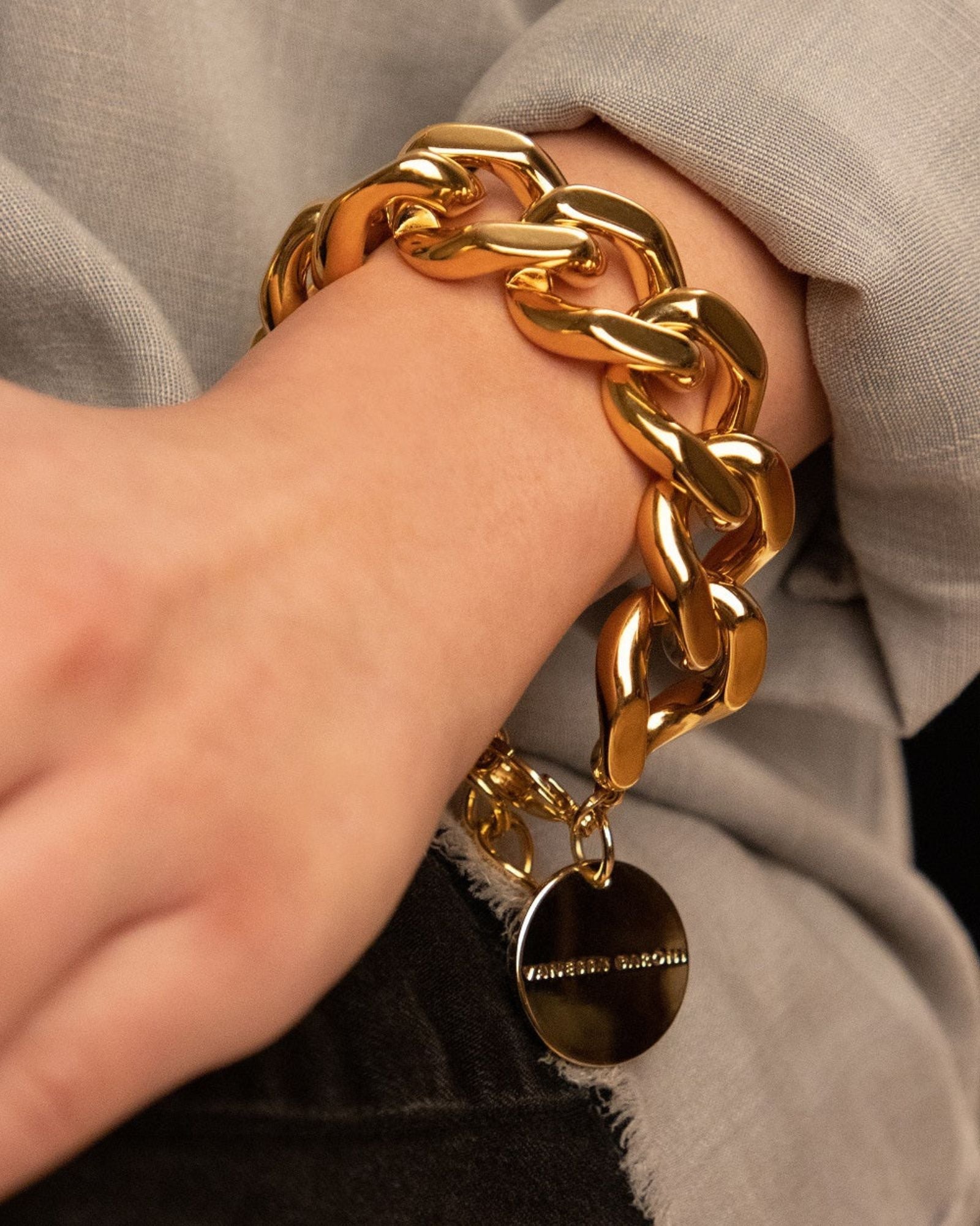 Woman wearing Vanessa Baroni's elegant gold flat chain bracelet, showcasing a modern design with chunky links and a secure gold clasp.