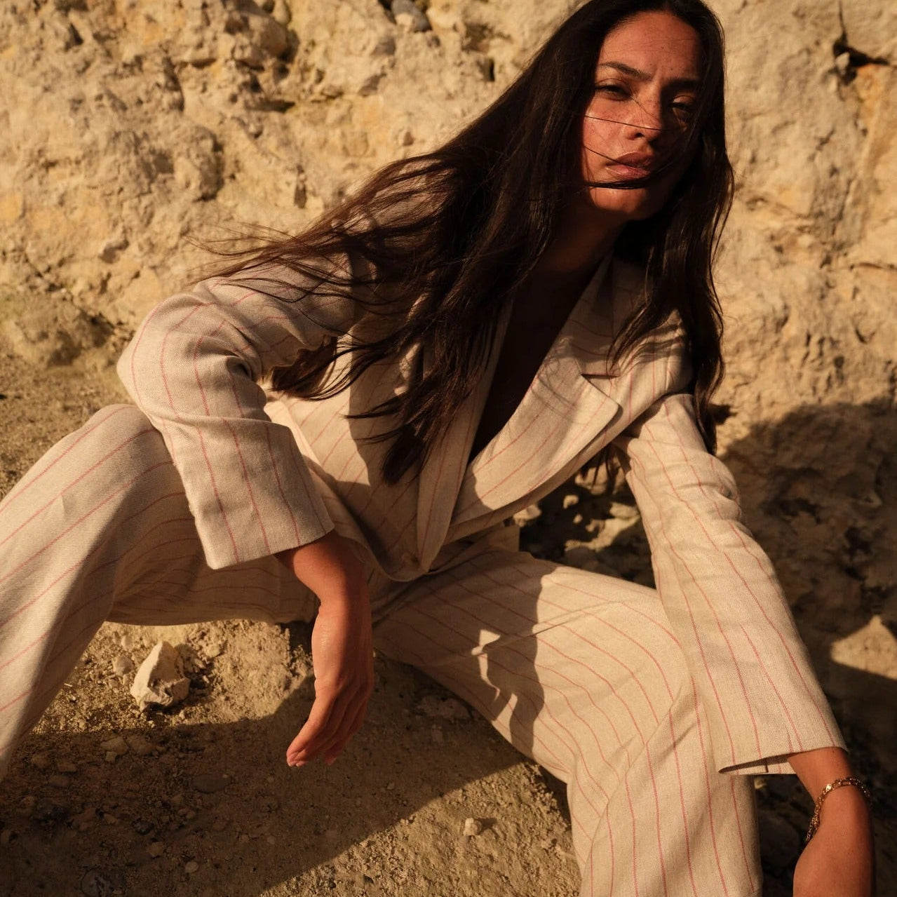Mos Mosh summer collection – woman in tailored striped suit in sunlit natural setting.