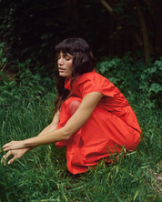 Model leaning wearing MMAria Mono Dress in Soft Coral, flowing midi-length skirt
