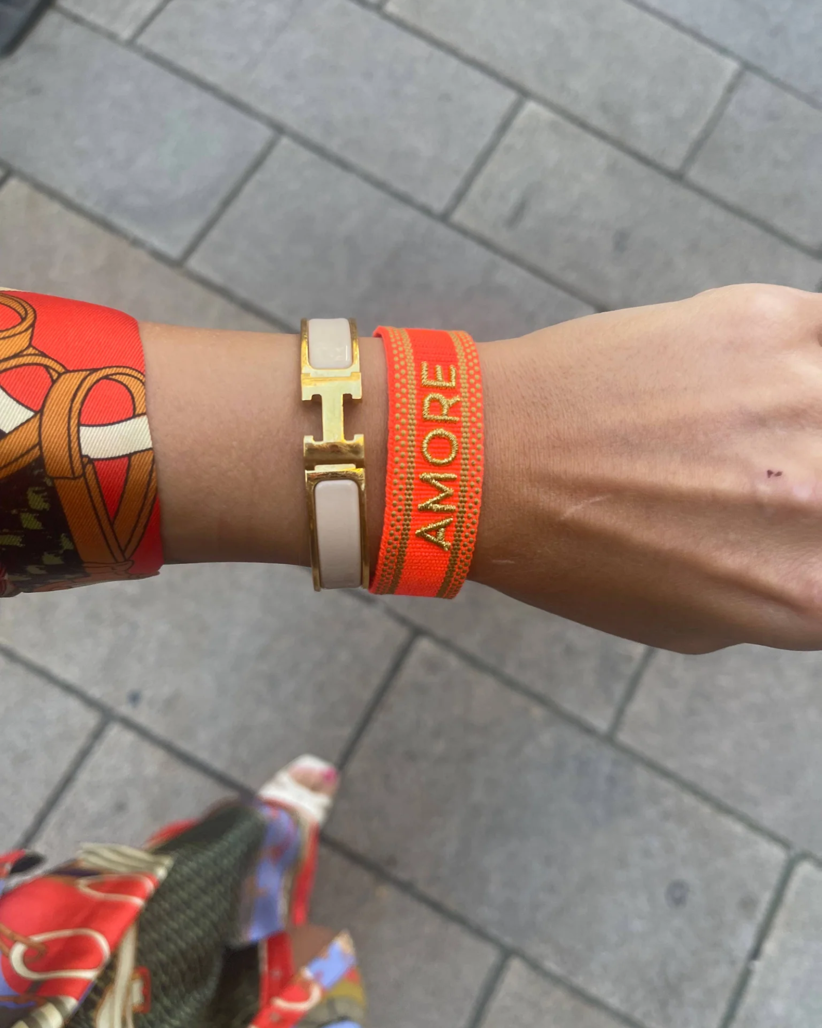 Close-up of adjustable neon orange woven friendship bracelet with green border and gold embroidered "AMORE" lettering and sliding knot cords.