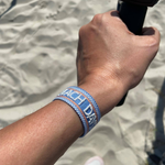 Close-up of adjustable blue woven friendship bracelet with off-white and orange border and embroidered "BEACH DAYS" lettering with sliding knot cords.