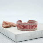 Close-up of adjustable vintage rose woven bracelet with embroidered “BELIEVE IN YOURSELF” lettering and sliding knot tassel cords.
