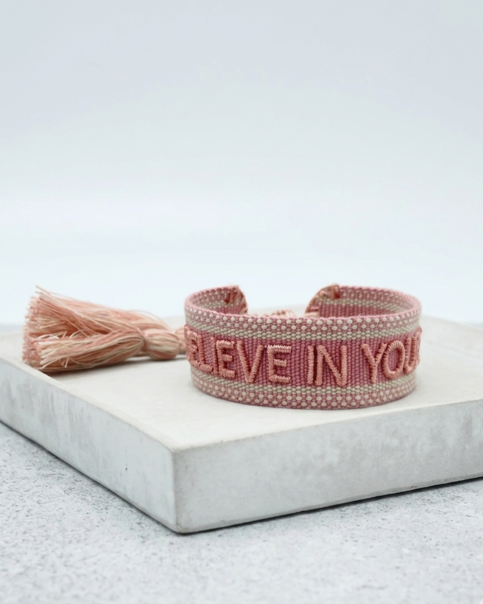 Close-up of adjustable vintage rose woven bracelet with embroidered “BELIEVE IN YOURSELF” lettering and sliding knot tassel cords.