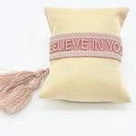 Close-up of adjustable vintage rose woven bracelet with embroidered “BELIEVE IN YOURSELF” lettering and sliding knot tassel cords.