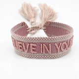 Close-up of adjustable vintage rose woven bracelet with embroidered “BELIEVE IN YOURSELF” lettering and sliding knot tassel cords.