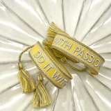 Close-up of adjustable sunshine yellow woven bracelet with embroidered “DO IT WITH PASSION” lettering and sliding knot tassel cords.