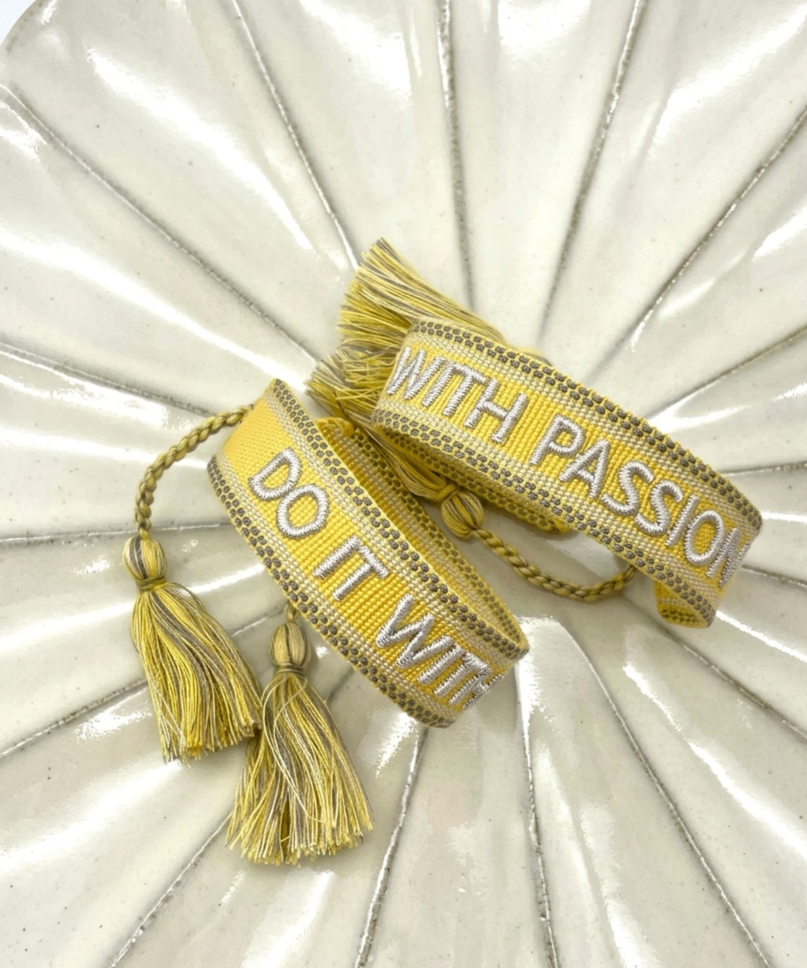 Close-up of adjustable sunshine yellow woven bracelet with embroidered “DO IT WITH PASSION” lettering and sliding knot tassel cords.