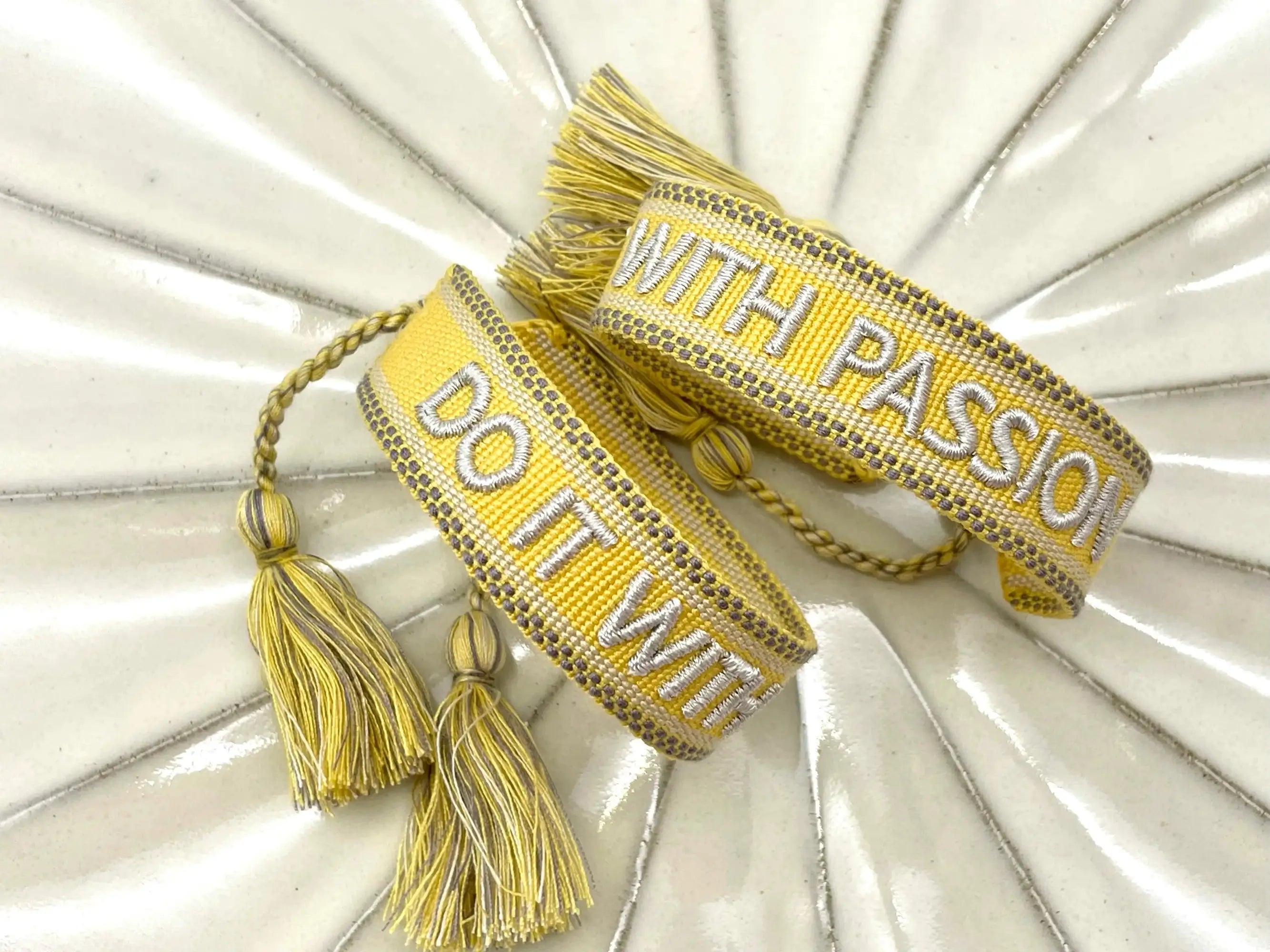 Two views of a bright yellow embroidered motivational quote bracelet on white ceramic.