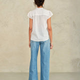 Person wearing a white blouse and blue jeans against a plain background