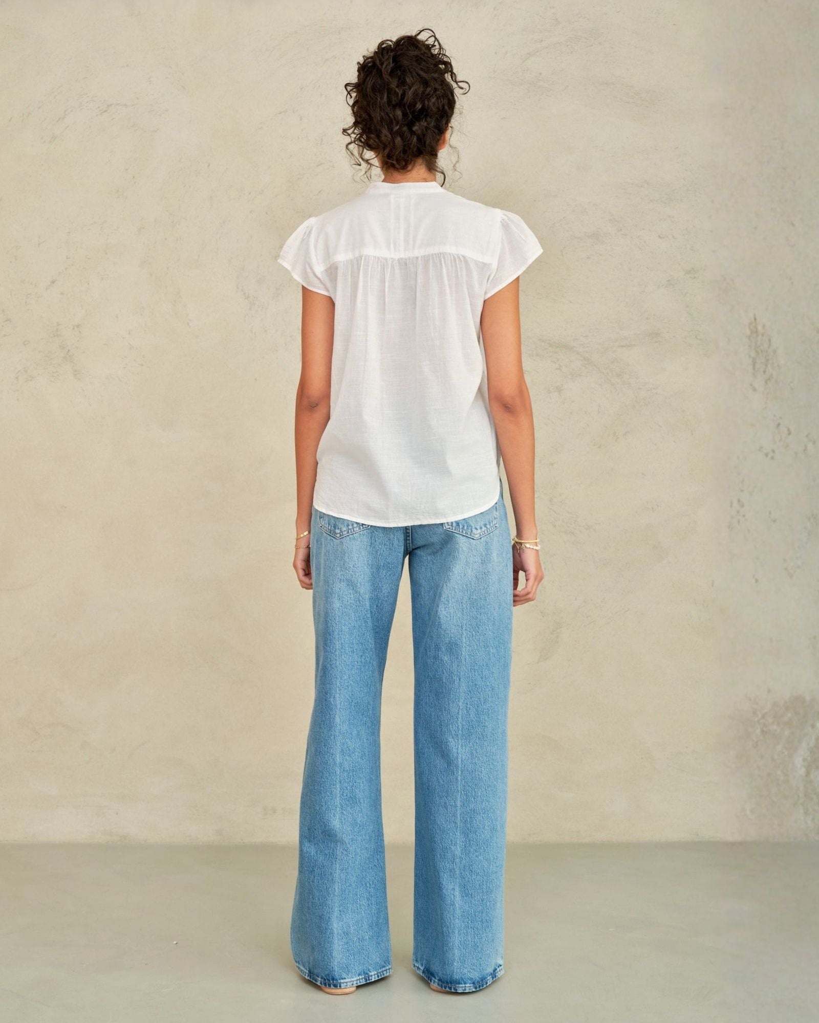 Person wearing a white blouse and blue jeans against a plain background