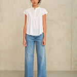 Woman wearing a white blouse and blue jeans against a plain background