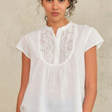 Woman wearing a white blouse with lace details against a neutral background