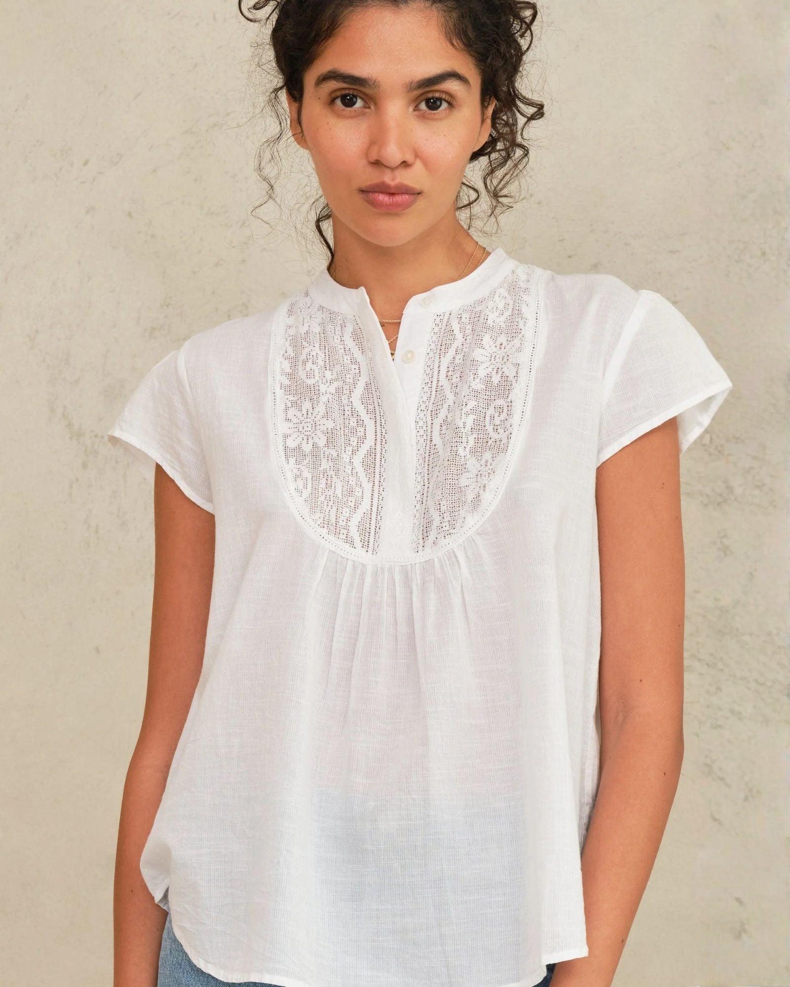 Woman wearing a white blouse with lace details against a neutral background