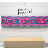 Close-up of adjustable turquoise woven friendship bracelet with pink border and embroidered "IBIZA IBIZA IBIZA" lettering with sliding knot cords.