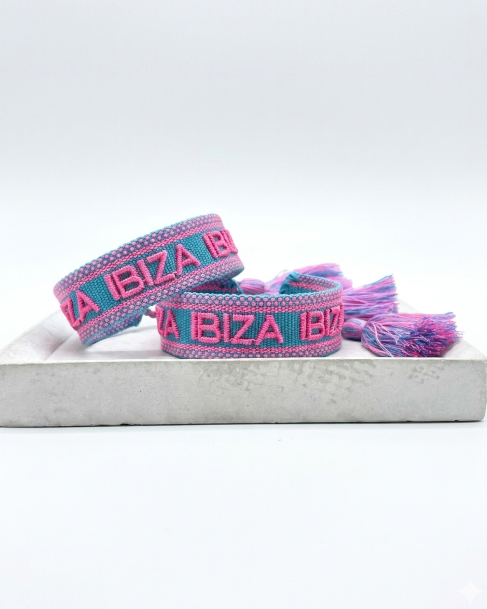 Close-up of adjustable turquoise woven friendship bracelet with pink border and embroidered "IBIZA IBIZA IBIZA" lettering with sliding knot cords.