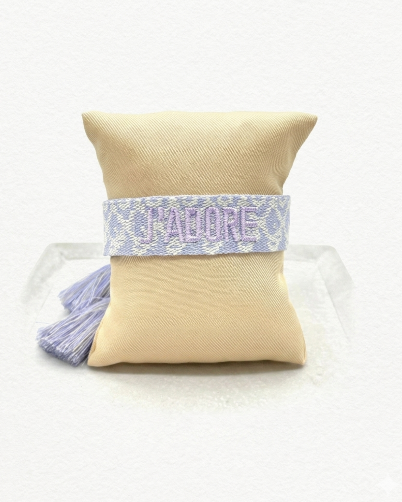Close-up of adjustable purple and cream jacquard woven friendship bracelet with lilac embroidered “J’ADORE” lettering and sliding knot tassel cords.