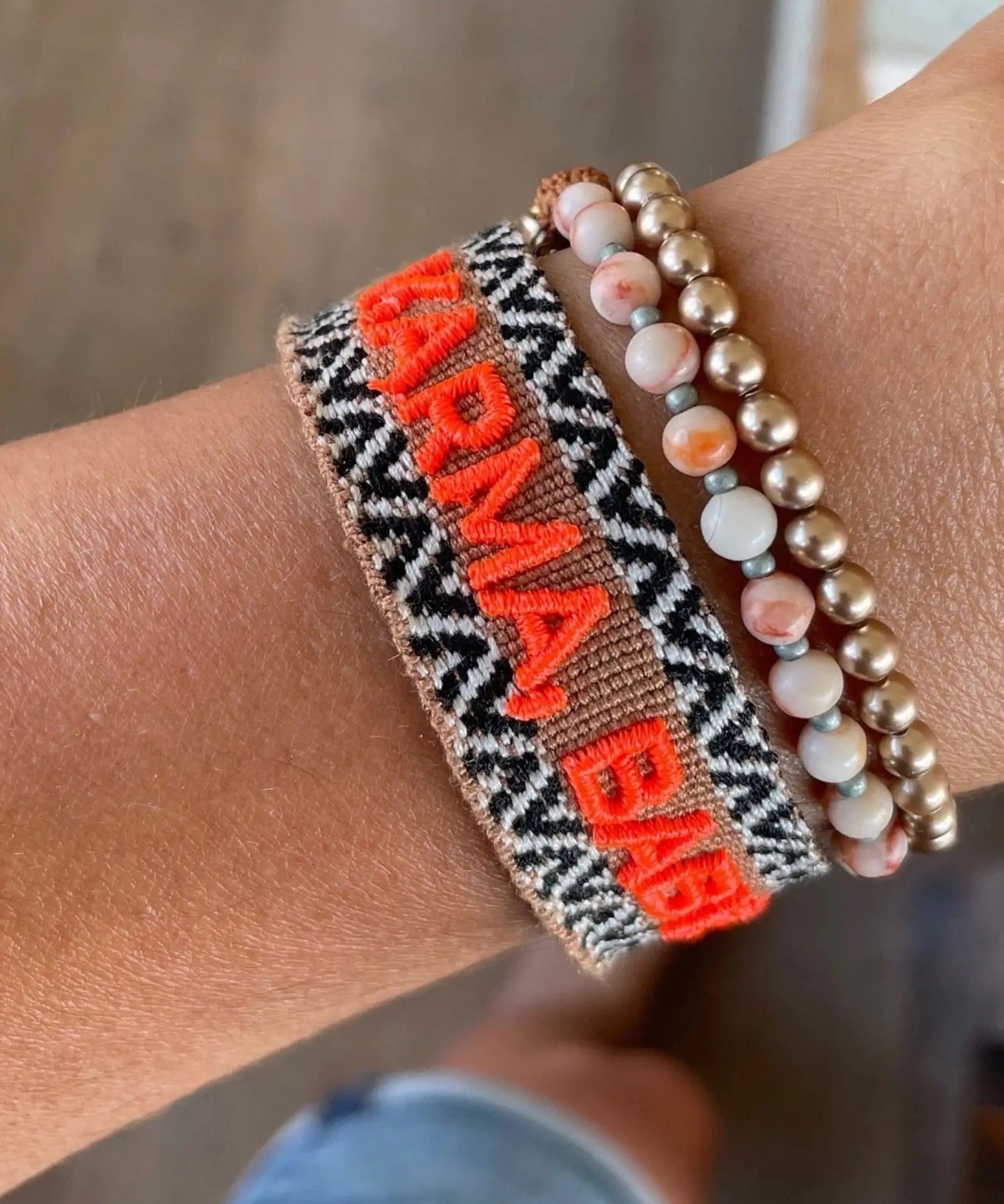 Close-up of adjustable woven boho friendship bracelet with neon orange “Karma, Baby!” embroidery and sliding tassel cords on a brown woven band.