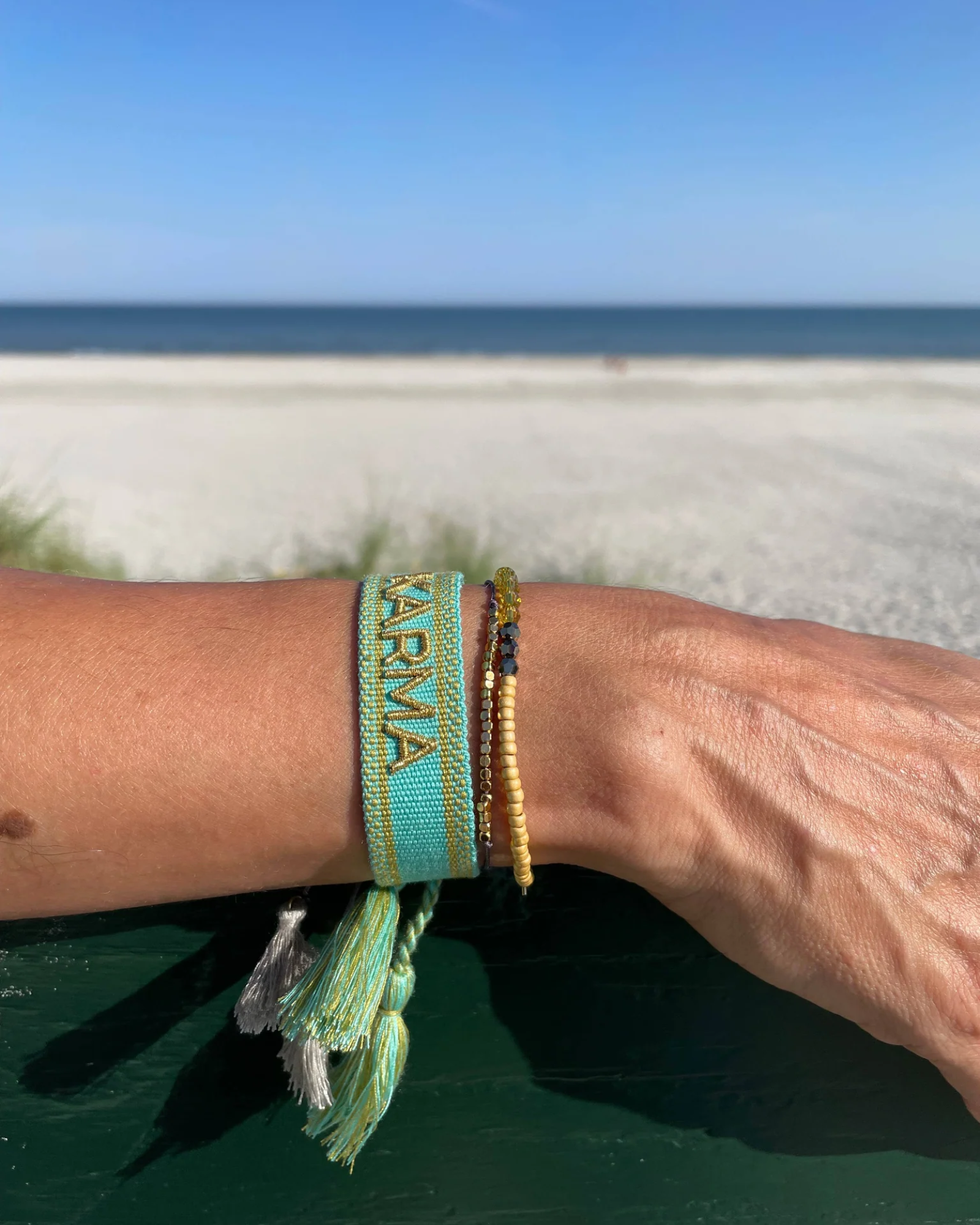 Close-up of adjustable turquoise woven bracelet with gold embroidered “KARMA” lettering and sliding knot tassel cords.