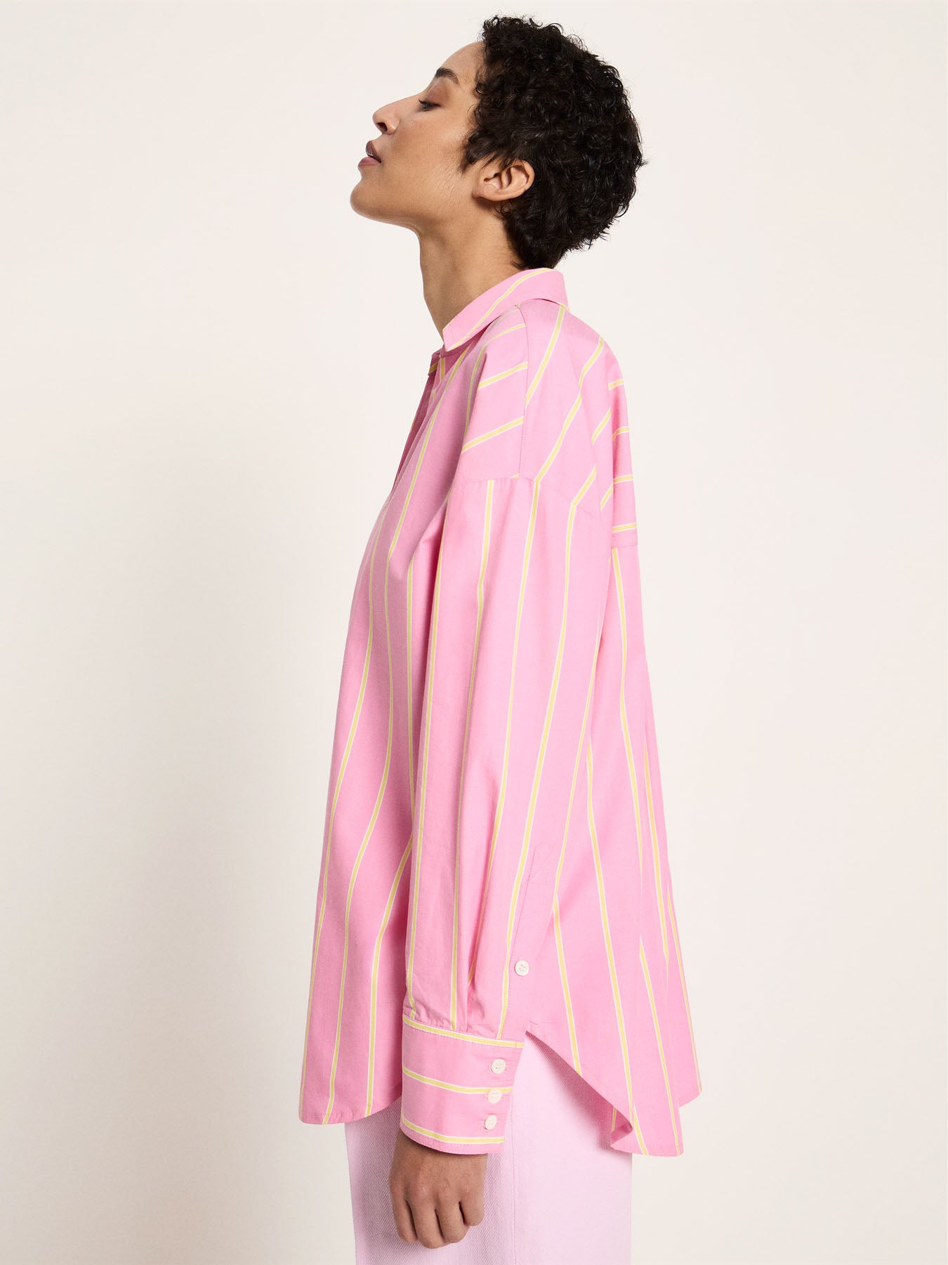 Side profile view showcasing the dropped shoulders, wide sleeves, and the fluid drape of the crisp organic cotton striped shirting fabric.