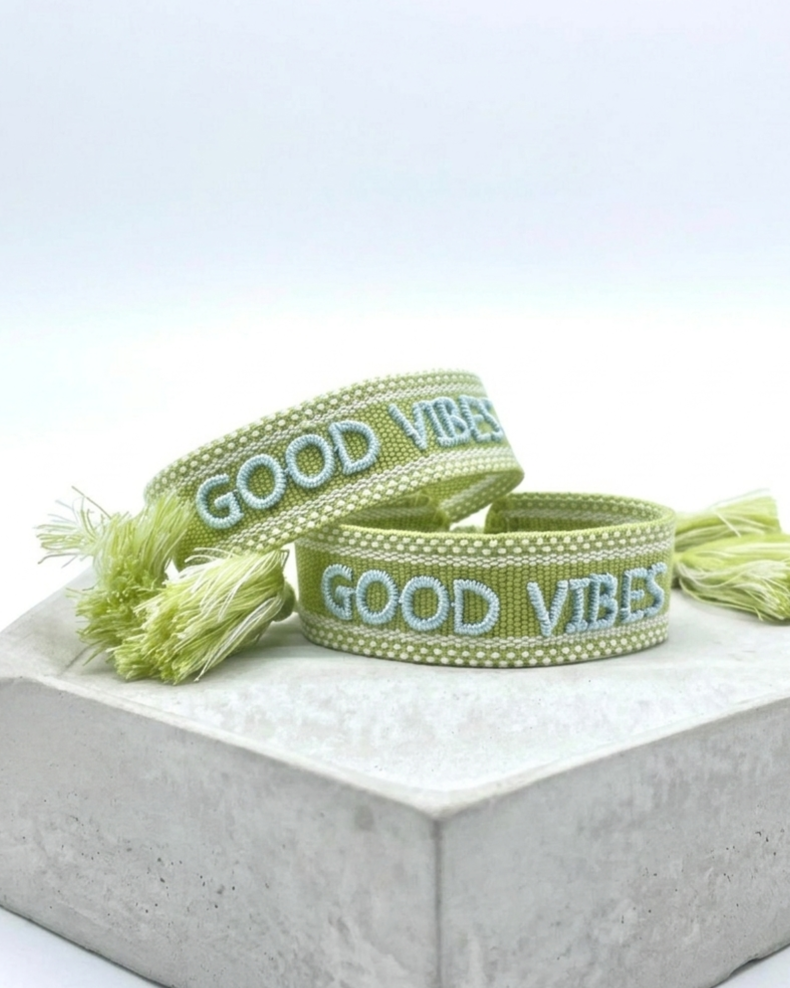 Close-up of adjustable cornflower blue woven bracelet with embroidered “LIVE LOVE SHINE” lettering and sliding knot tassel cords.