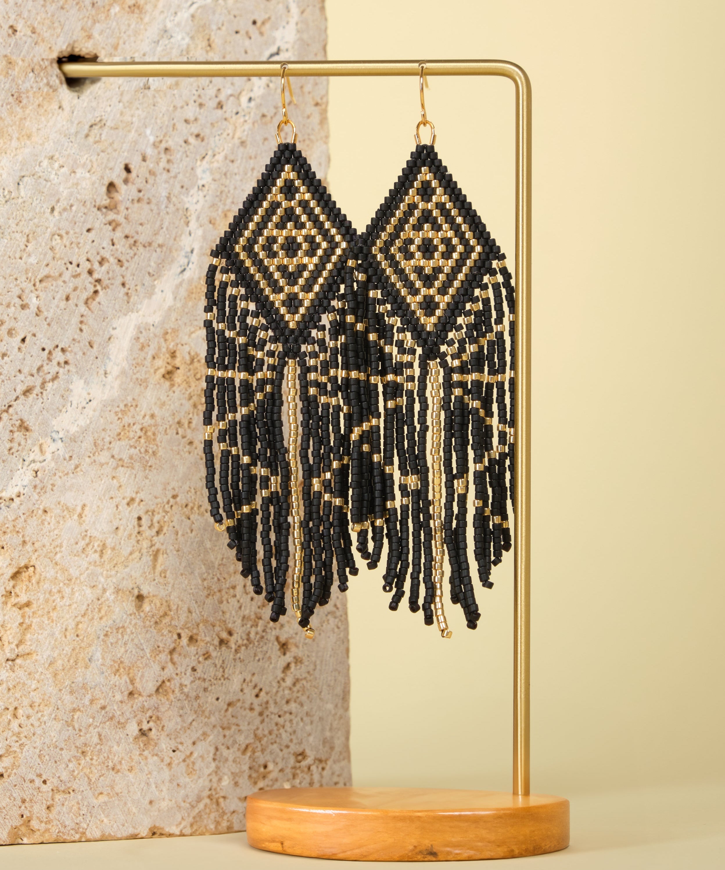 Tribal Diamond Fringe Earrings in Black/Gold – Elegant beaded earrings displayed on a textured jewelry stand