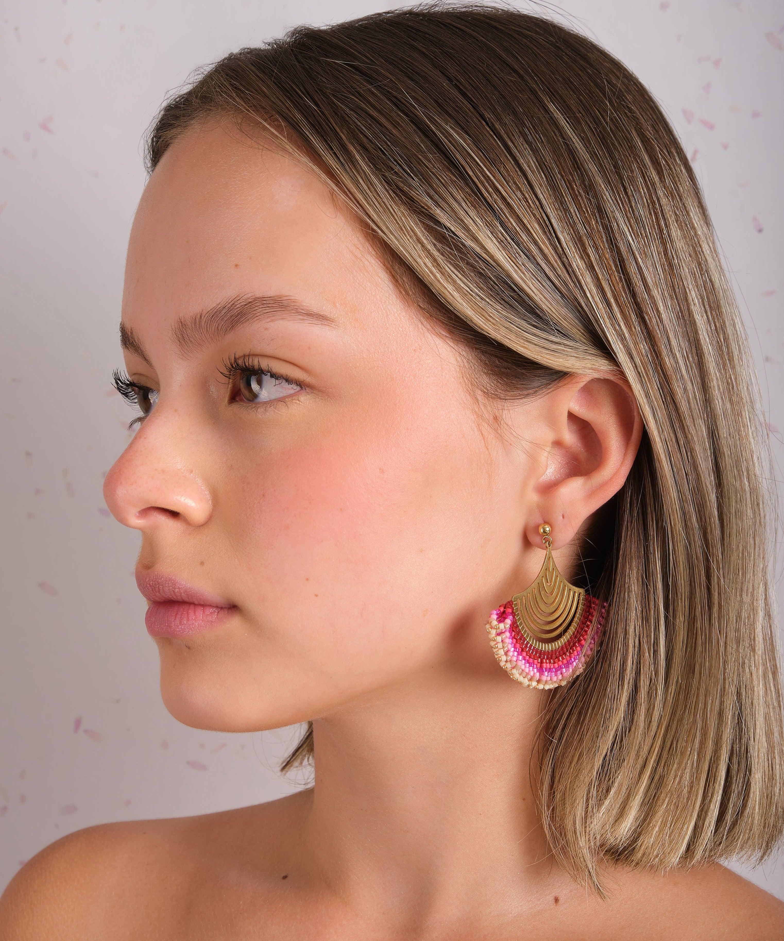 Woman wearing Mayana Designs Beaded Handwoven Flamenco Fan Earrings in Pink, profile view showcasing vibrant beadwork and brass accents