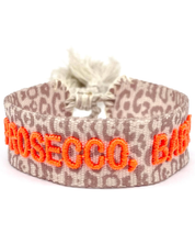 Close-up of adjustable woven friendship bracelet with Leo pattern and neon orange embroidered "PROSECCO, BABY!" lettering with sliding knot cords.