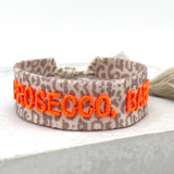 Close-up of adjustable woven friendship bracelet with Leo pattern and neon orange embroidered "PROSECCO, BABY!" lettering with sliding knot cords.