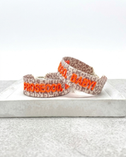 Close-up of adjustable woven friendship bracelet with Leo pattern and neon orange embroidered "PROSECCO, BABY!" lettering with sliding knot cords.