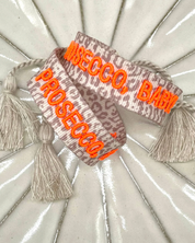 Close-up of adjustable woven friendship bracelet with Leo pattern and neon orange embroidered "PROSECCO, BABY!" lettering with sliding knot cords.