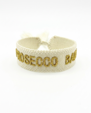 Close-up of adjustable ecru woven bracelet with gold embroidered “PROSECCO BABY” lettering and sliding knot tassel cords.
