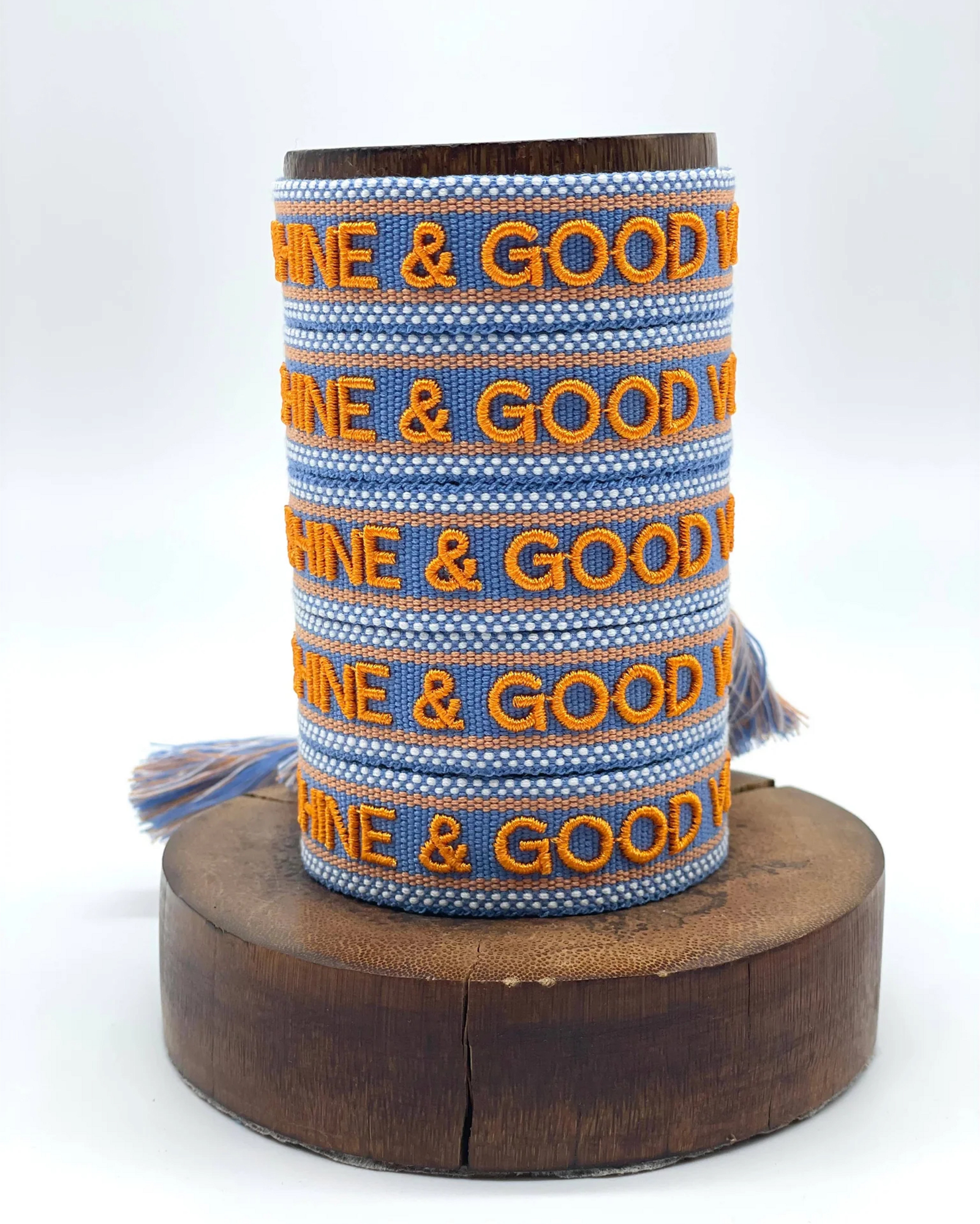 Close-up of adjustable blue and orange woven friendship bracelet featuring embroidered "SUNSHINE & GOOD VIBES" lettering and sliding knot tassel cords.