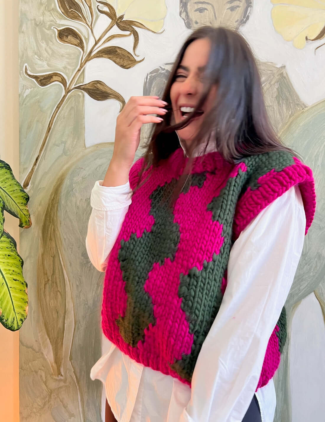 Modeal wears ethically crafted knitted vest with wave design in Hot Pink & Heritage Green – over white shirt - perfect for layering.