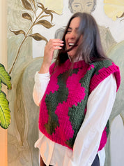 Modeal wears ethically crafted knitted vest with wave design in Hot Pink & Heritage Green – over white shirt - perfect for layering.