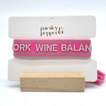 Close-up of adjustable pink woven bracelet with silver gray embroidered “WORK WINE BALANCE” lettering, matching border, and sliding knot tassel cords.