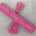 Close-up of adjustable pink woven bracelet with silver gray embroidered “WORK WINE BALANCE” lettering, matching border, and sliding knot tassel cords.