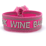 Close-up of adjustable pink woven bracelet with silver gray embroidered “WORK WINE BALANCE” lettering, matching border, and sliding knot tassel cords.