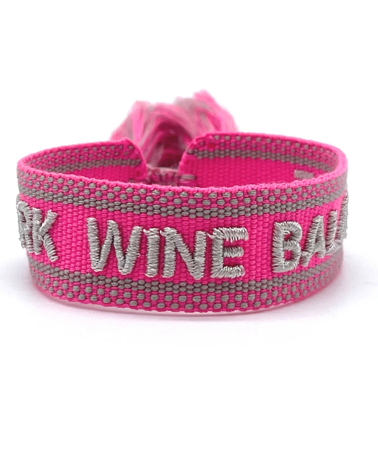 Close-up of adjustable pink woven bracelet with silver gray embroidered “WORK WINE BALANCE” lettering, matching border, and sliding knot tassel cords.
