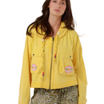 A woman wearing the vibrant yellow Amy cotton zip-up hooded jacket with cargo chest pockets and colorful beaded drawstring details.