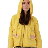 Front studio view of a model with the hood up on the washed yellow Amy cotton jacket, showcasing its straight silhouette.