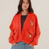 A woman facing forward wearing the oversized red acid-washed Azellia cotton jacket with large utility pockets and decorative front patches.