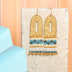 Vibrant Blue Aqua Miyuki glass beads and cream beads hang from a brass arch, creating a playful and stylish earring. 