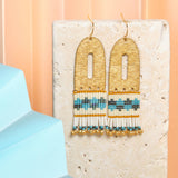 Vibrant Blue Aqua Miyuki glass beads and cream beads hang from a brass arch, creating a playful and stylish earring. 