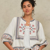 Model wearing an open-front Mabe Apparel embroidered cotton jacket with white trousers.