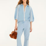 Full-length studio shot of a model styling the Farm Rio bicolor blue denim blouse with matching denim pants, holding a textured brown handbag.
