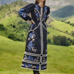 Full-length outdoor lifestyle view of a model in the Farm Rio Black Bold Flowers midi dress, paired with boots in a scenic green landscape.