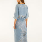 Back view of a model in a studio showcasing the high-rise fit and embroidery details of the FARM Rio denim midi skirt.